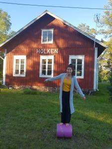 a woman standing on a suitcase in front of a house at Cirkus Hostel Holken in Inkoo
