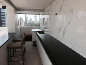 a white kitchen with a black counter and a window at Manaíra Apart Hotel in João Pessoa
