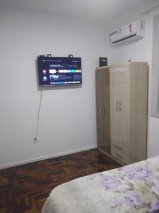 a room with a tv on the wall and a cabinet at Quarto exclusivo em APTO compartilhado in Novo Hamburgo