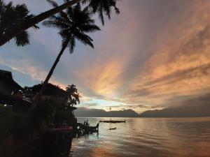 een zonsondergang boven een waterlichaam met palmbomen bij Beach Guest House in Maninjau