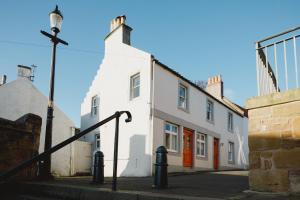 a white building with an orange door on a street at The Crow's Nest in Pittenweem