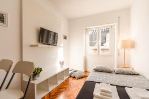 a white bedroom with a bed and a tv on the wall at Carmo Apartments in Lisbon