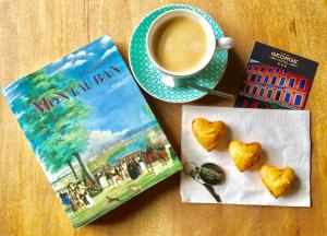 un livre et une tasse de café à côté d'un biscuits en forme de cœur dans l'établissement Hôtel du Commerce, à Montauban