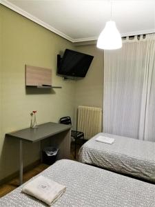 a room with two beds and a tv on the wall at Pension Santiago in Burgos