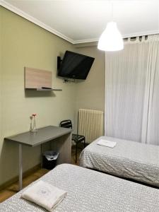 a room with two beds and a tv on the wall at Pension Santiago in Burgos