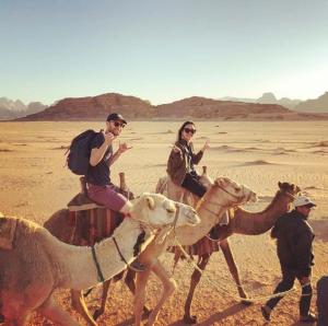 a group of people riding on camels in the desert at moon city camp with sunrise in Wadi Rum
