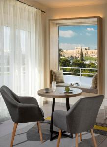 ein Wohnzimmer mit einem Tisch, Stühlen und einem Fenster in der Unterkunft Acropolis View Homey #1 in Athen