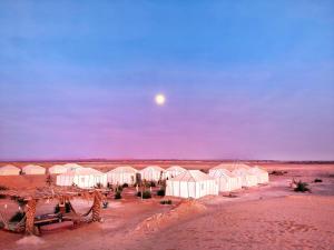 a view of a desert with houses and the moon at Sahara Majestic Luxury Camp in Merzouga