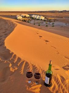 a bottle of wine and two glasses on the beach at Sahara Majestic Luxury Camp in Merzouga
