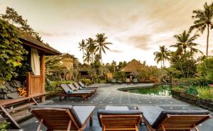 a resort with a pool and chairs and palm trees at Tanah Merah Art Resort in Ubud