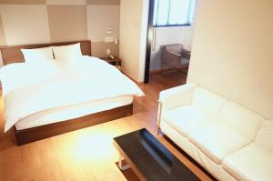 1 dormitorio con cama blanca y sofá en LUXe, en Higashihiroshima