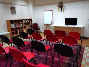 a classroom with red chairs in a room with a screen at Ostello Angolo Verde in Angolo Terme