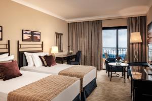 a hotel room with two beds and a desk at Corinthia St George's Bay in St. Julianʼs