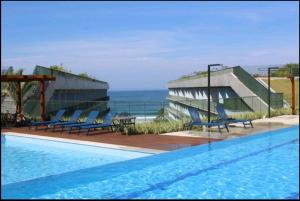 a swimming pool with chairs and the ocean in the background at Maravilhoso Apartamento Reserva DNA Ubatuba in Ubatuba