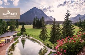 a house with a pond in a field with a mountain at Alpenhotel Karwendel -Adults only- in Leutasch