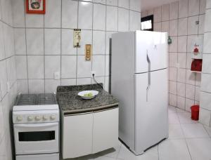 a white kitchen with a stove and a refrigerator at Apartamento Residencial Angélica em Guarapari a 150m do mar in Guarapari