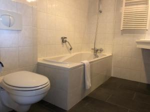 a white bathroom with a toilet and a bath tub at Strandhotel Om de Noord in Schiermonnikoog