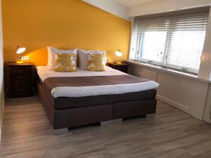 een slaapkamer met een bed met gele muren en 2 ramen bij Strandhotel Om de Noord, logies en ontbijt in Schiermonnikoog