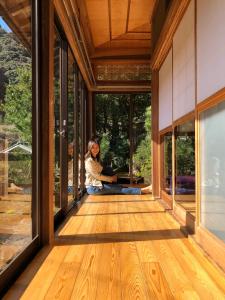 a woman sitting on the floor of a room with windows at Shimanto Riverside Hideaway in Shimanto
