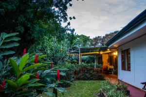 a garden with red flowers and a house at Hotel La Rosa de America in Alajuela City