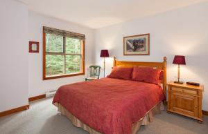 a bedroom with a bed with a red comforter and a window at Treeline Townhome by Whistler Premier in Whistler