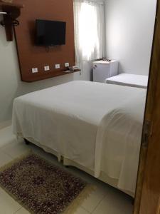 a bedroom with a large white bed with a television at Hotel Itamarati in Uberlândia