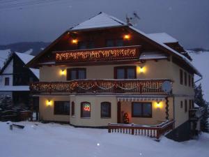 une maison avec une terrasse dans la neige la nuit dans l'établissement Penzion Deny, à Ždiar