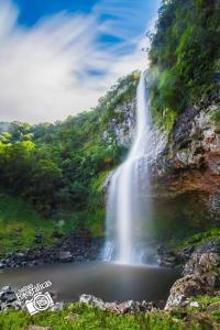 a waterfall on the side of a mountain next to a lake at Pousada Três Forquilhas in Guananazes