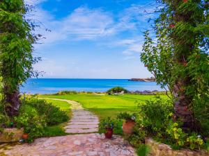 a path through a garden with the ocean in the background at Kounopetra Beach Luxury Villas in Kounopetra