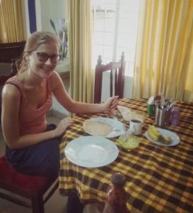 a woman sitting at a table with plates of food at Frangipani Holiday Home in Fort Kochi