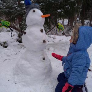 una niñita construyendo un muñeco de nieve en la nieve en Hakuba Cottage Gram, en Hakuba