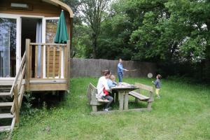 een vrouw en kinderen die spelen aan een picknicktafel in een tuin bij Camping le Nid du Parc in Villars-les-Dombes