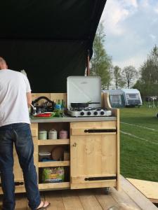 un homme debout devant une cuisine sous une tente dans l'établissement Safaritent de Berghoeve, à Ruinen