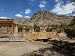 a wooden bridge in a village with mountains in the background at Ladakh Eco Resort in Leh
