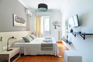 a white bedroom with a bed and a television at Aegle by Heloni Apartments in Athens