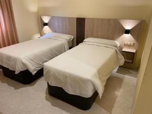 two beds in a hotel room with white sheets at Hotel La Parada in Ontígola