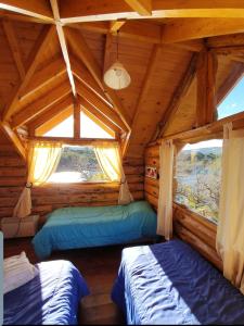 two beds in a log cabin with two windows at costa bonita el bosque in Villa Pehuenia