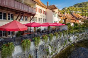 a restaurant with tables and red umbrellas next to a river at Hotel Demi-Lune in Saint-Ursanne