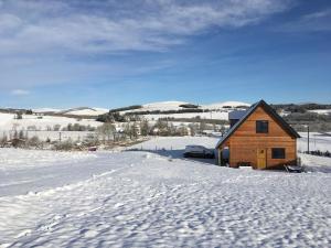 een houten huisje in de sneeuw met een auto ernaast bij Isla Pod, Kilry eco pods in Blairgowrie