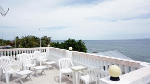 a balcony with white chairs and tables and the ocean at Cronin Residences in Oslob