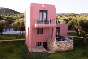 a pink house with a balcony in the grass at Blue Waves Houses in Plomarion