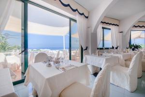un ristorante con tavoli e sedie bianchi e finestre di Paradiso Terme Resort & SPA con 5 piscine termali a Ischia