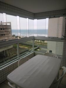 - une table et des chaises blanches dans une chambre dotée d'une grande fenêtre dans l'établissement Apartamento para temporada Condomínio Ilha de Noronha Praia Grande SP, à Praia Grande