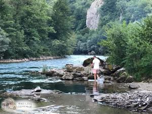 un hombre parado en el agua en un río en Exo Log Cottage en Jezero