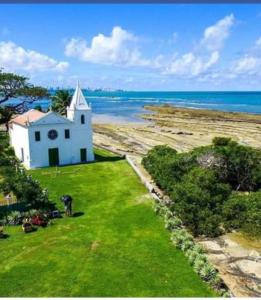 a white church on a field of grass next to the ocean at Pousada Odemir Ferreira in Vera Cruz de Itaparica