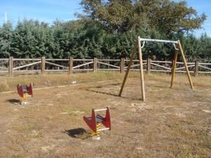 three swings in a field next to a fence at ALBERGUE TURÍSTICO DE CORNALVO in Trujillanos