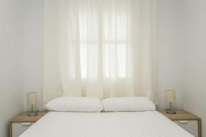 a bedroom with a white bed with two lamps at Apartamentos Los Cantaros in El Puerto de Santa María