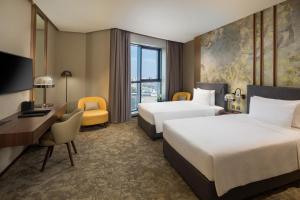 a hotel room with two beds and a desk at Millennium Place Barsha Heights Hotel in Dubai