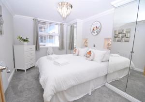 a white bedroom with a large white bed and a chandelier at Twenty Three B - 3 bedroomed apartment in Lee-on-the-Solent