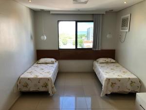 two beds in a room with a window at Apartamento amplo, arejado e confortável - Mínimo 3 noites in Ilhéus